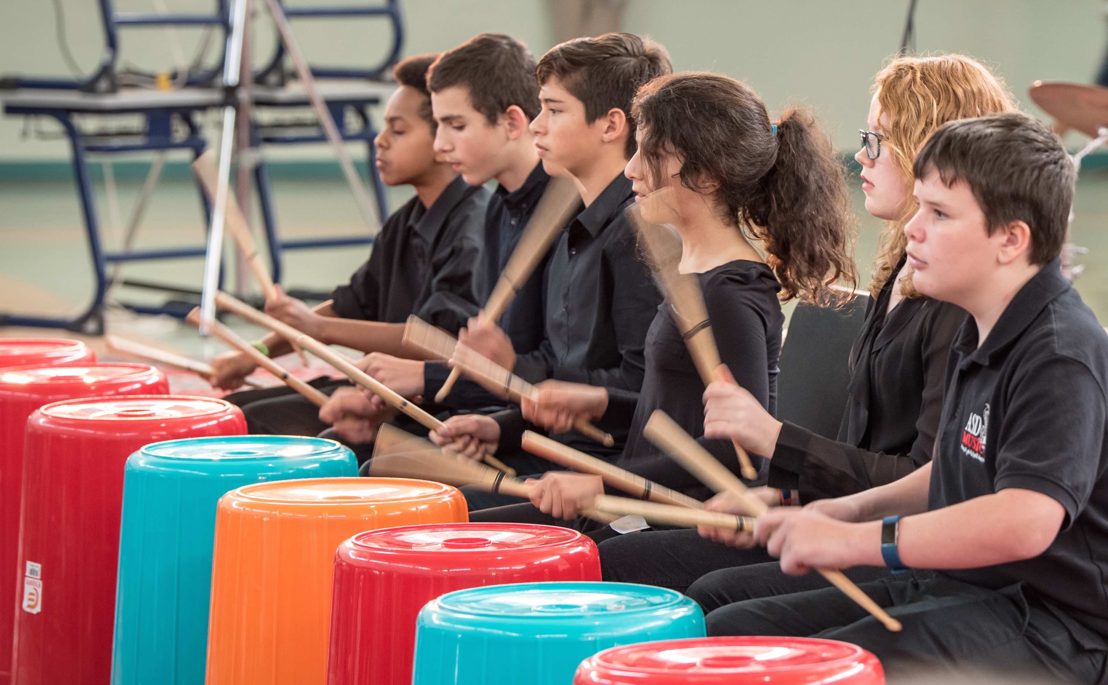 Students performing coordinated rhythms on colourful bucket drums